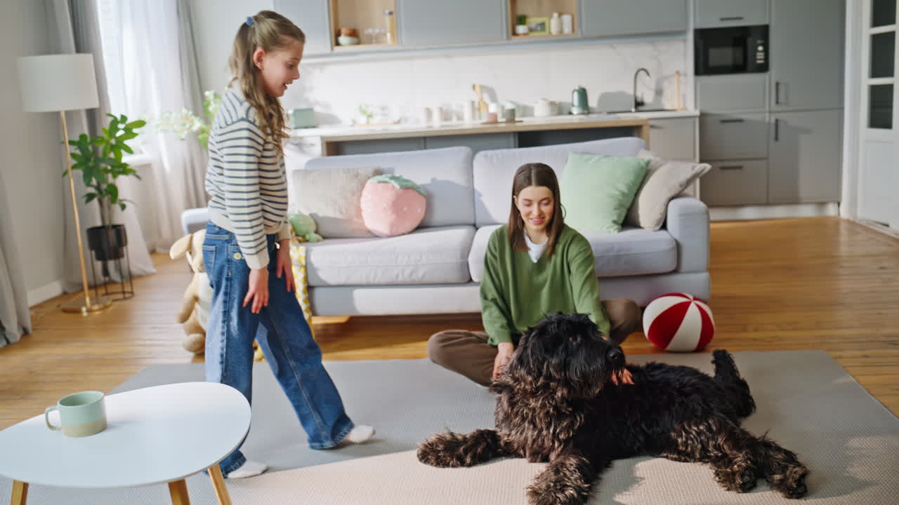 Mor, datter og leken hund tilbringer tid sammen i stuen. Kjæledyret ligger på teppet.