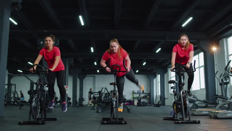 healthy caucasian group of women exercising workout on stationary cycling machine bike in gym