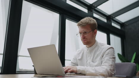 inside office of serious businessman handsome man is working with laptop in room sending message