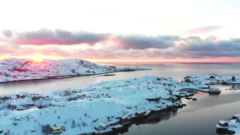 drone view of a snowy landscape on the lofoten islands with the sunrise at the background and some clouds