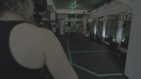 una toma deslizante de una mujer blanca haciendo ejercicio en una bicicleta estática dentro de un gimnasio