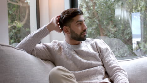 Portrait-of-happy-biracial-man-sitting-on-sofa-smiling-at-home,-slow-motion