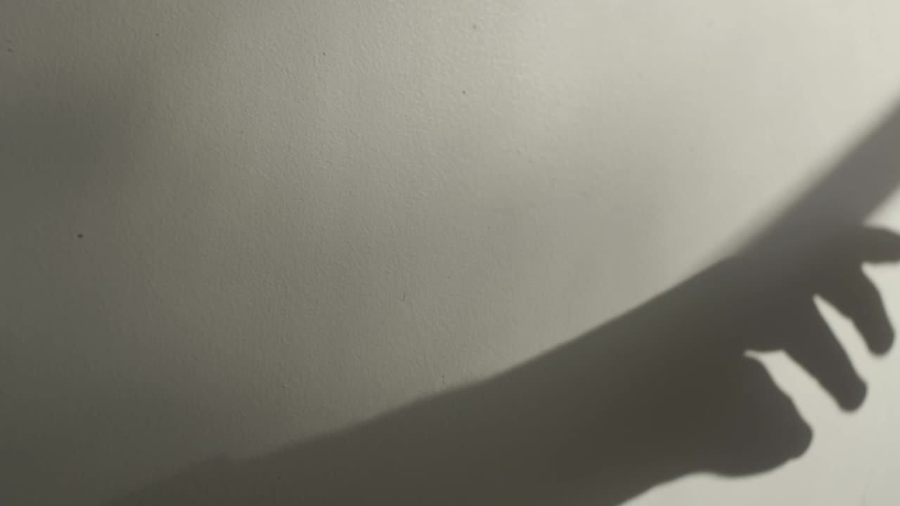 창에서 단단한 그림자가 있는 흰색 벽 위로 손이 전달됩니다.