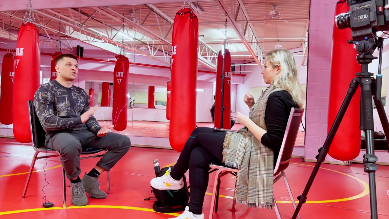 New York, ABD, 9 Mart 2022: Kum Torbalarıyla Boks Salonunda Video Röportaj Kurulumu. Kırmızı kum torbaları, tripod kamera, mikrofonlar ve pembe aydınlatma ile donatılmış boks salonunda röportaj için oturan iki yetişkin.
