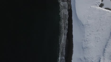 Von-Oben-Nach-Unten-Luftbild-Schneebedeckter-Strand-Mit-Schwarzen-Meereswellen-An-Der-Küste