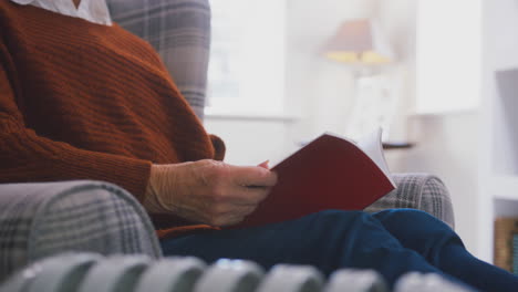 mujer mayor leyendo un libro calentándose con un radiador portátil en la crisis de energía del costo de la vida