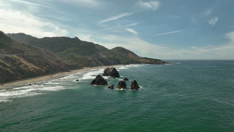 Aerial-view-of-large-rock-islands-popping-out-of-California's-colorful-coastline