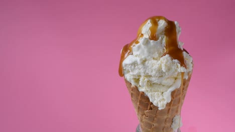 caramel sauce being poured over vanilla ice cream waffle cone on fun vibrant pink background