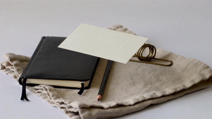 Sliding blank card entering, crossing pale table on beige linen, passing notebook pencil brass clip