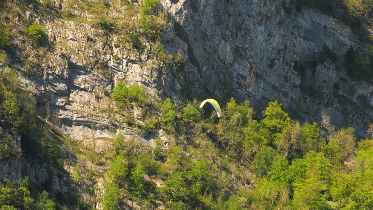 A person is paragliding with giant rocks in the background. The sun illuminates the beautiful nature and the landscape with its large rocks.