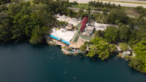 Wide-angle-drone-shot-of-the-famous-"Cenote-Azul"-with-many-people-going-for-a-swim-and-relaxing-located-outside-the-city-of-Bacalar,-Mexico-in-4k