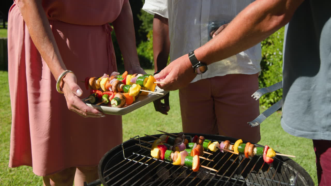 Grilling colorful vegetable skewers in garden, enjoying sunny day with diverse friends