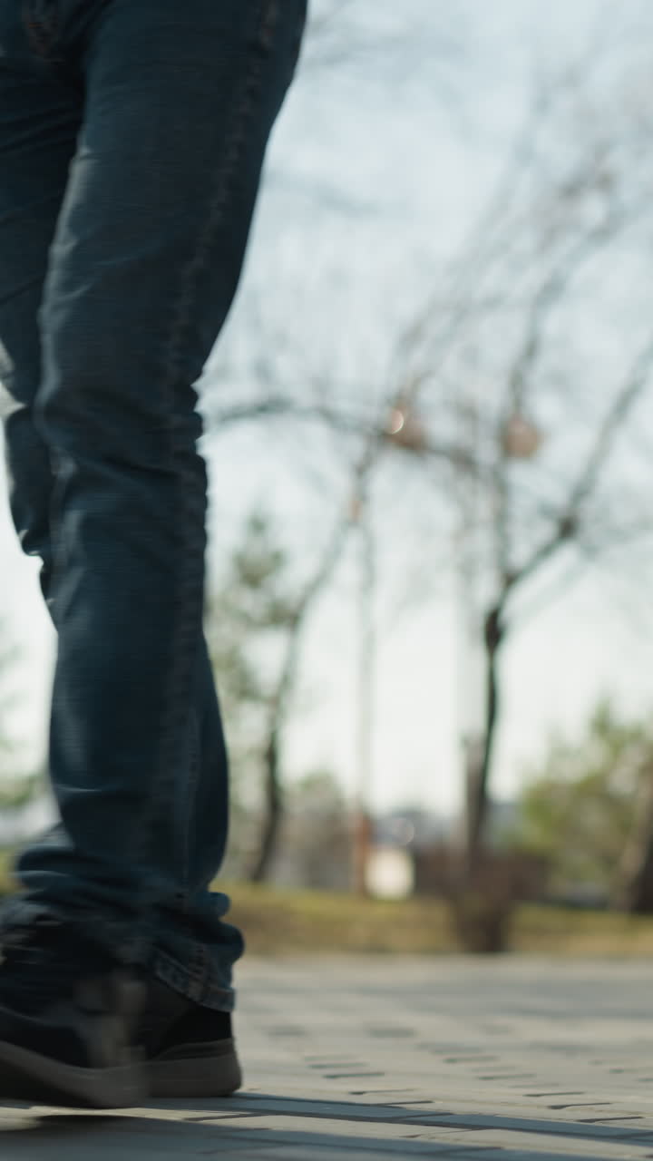 una vista cercana de una pierna de un adulto que lleva a un niño mientras camina por una calle, con árboles y un poste de luz a su alrededor y una vista borrosa de una ciudad detrás de él