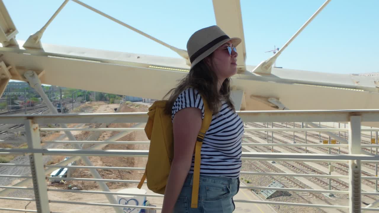 A woman is walking with a green suitcase on a bridge.