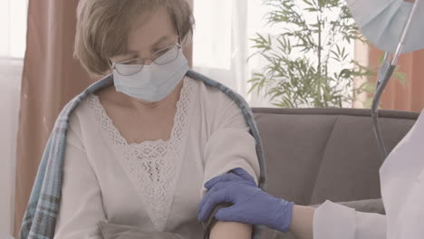 Female-Doctor-Takes-The-Pulse-Of-An-Elderly-Patient-Sitting-On-A-Sofa-3