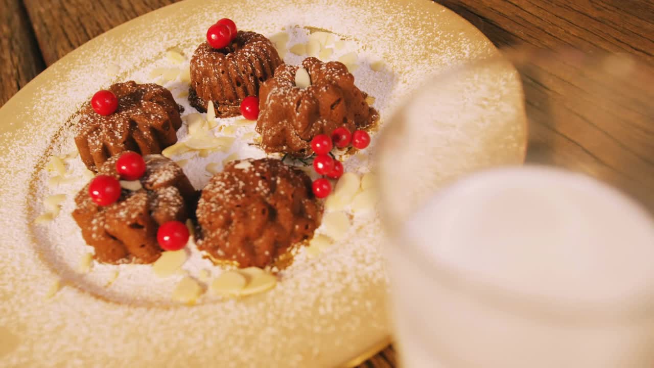 Sparkles drifting over chocolate bundt cakes dusted with sugar, camera panning to reveal milk glass