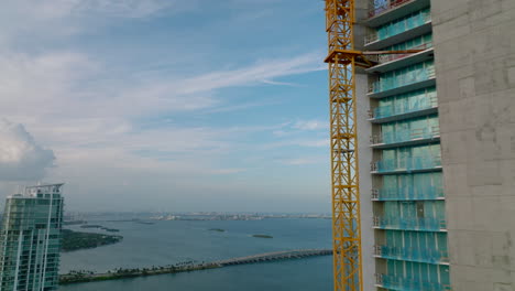 Volar-Alrededor-De-La-Construcción-De-Un-Nuevo-Rascacielos.-Reveladora-Vista-Panorámica-De-La-Bahía-Del-Mar-Y-Los-Aviones-En-El-Cielo.-Miami,-Estados-Unidos