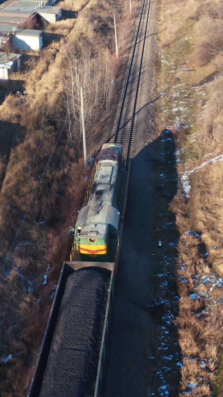 Cargo train on a railroad in sunny winter day. Top view on a freight train on the background of many garages from both sides. Aerial view. Vertical video