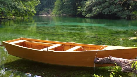 Bote-Pequeño-De-Madera-Flotando-En-La-Superficie-De-Un-Agua-Reflectante-Cristalina-Y-Tranquila