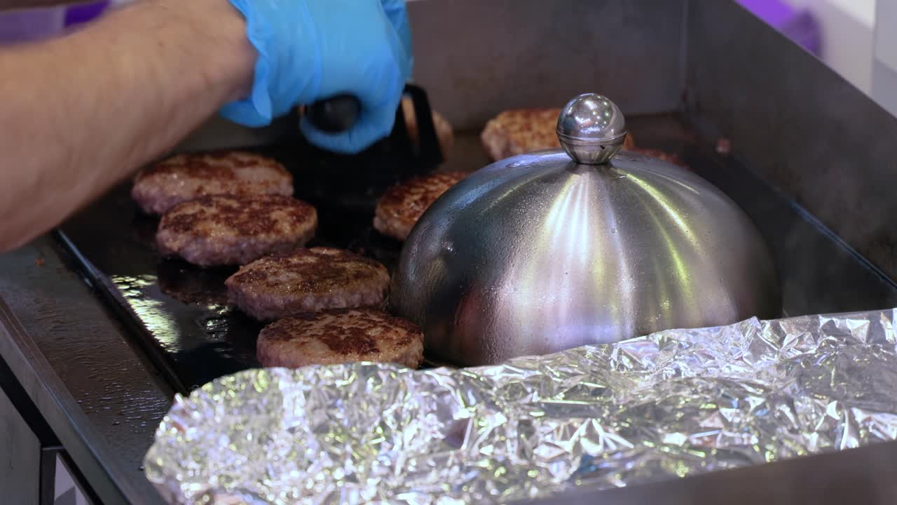 Un hamburger di carne si cucina in una padella calda e rovente. Cibo da strada, lo chef gira gli hamburger con una spatola.