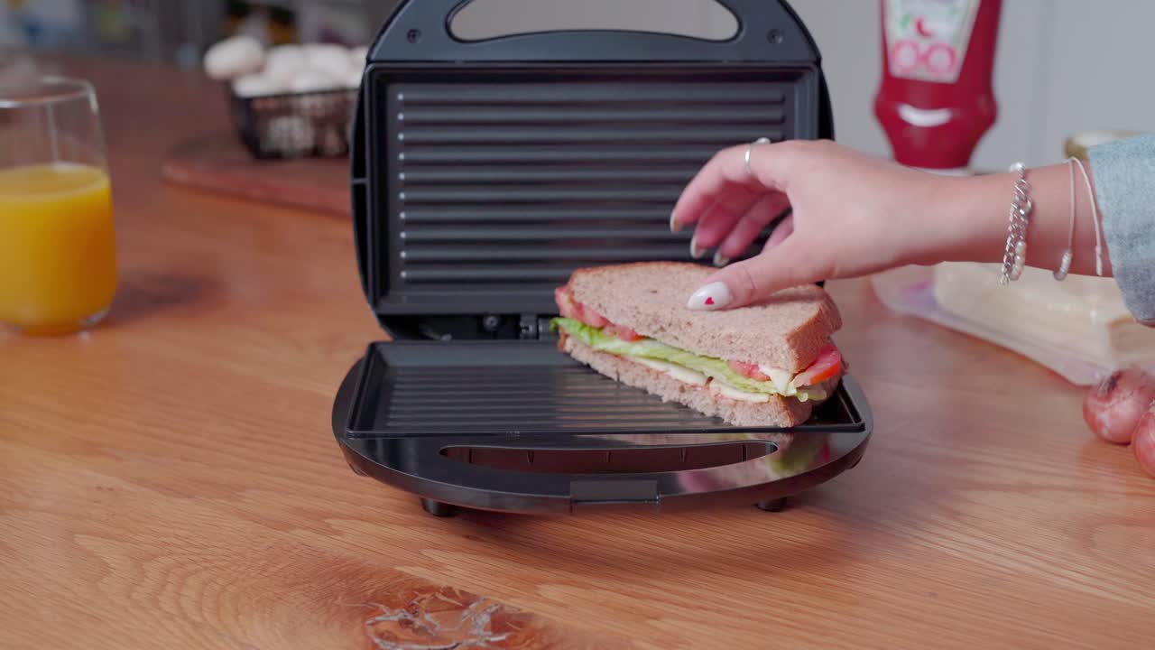 Donna che mette un panino con lattuga, pomodoro e formaggio a fette sulla piastra elettrica