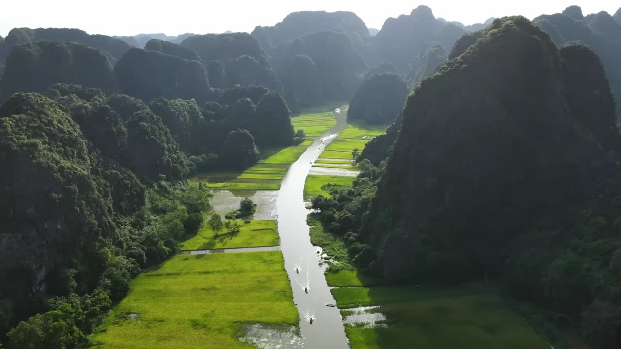Drone photo of a scenic river snaking through lush valleys and rice paddies, framed by dramatic limestone cliffs and tropical greenery in a peaceful landscape.