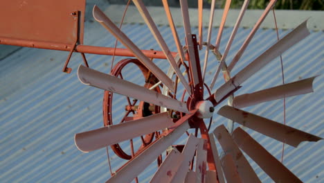 close up view of rust coloured spinning windmill with tin roofs in the background