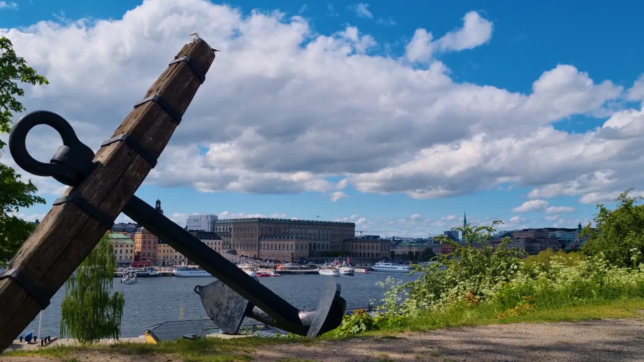View of a weathered anchor atop a hill, overlooking Gamla Stan and Strömmen Bay under a partly cloudy spring sky in Stockholm, Sweden