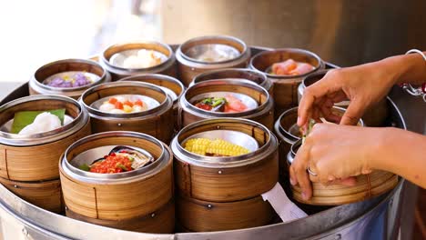 hands selecting dim sum from bamboo steamers in bright, natural light. captured in a bustling phuket market setting