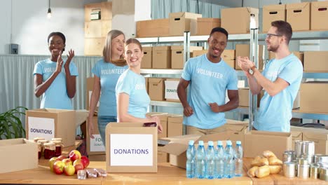 multiethnic group of volunteers standing in charity warehouse clapping hands and giving high five in charity warehouse