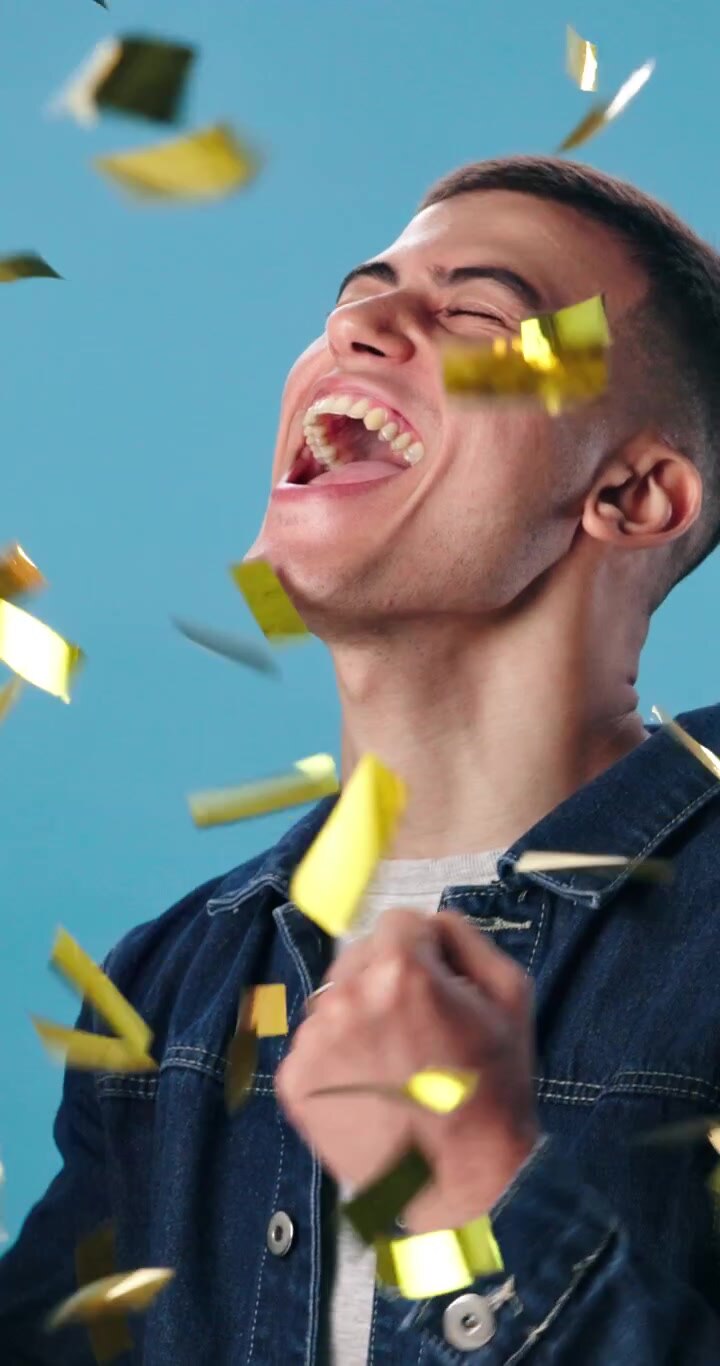 Giovane uomo entusiasta che festeggia il successo tra coriandoli dorati che cadono