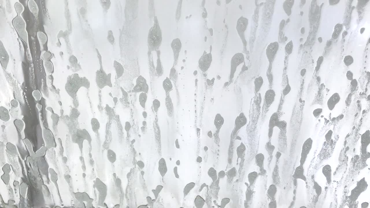 Driver's side window of car being sprayed with soap at an automatic car wash.