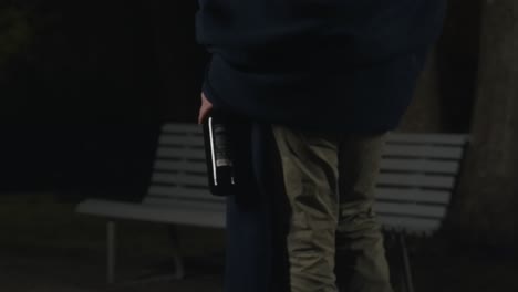 alcoholic walks through the park at night with a bottle in his hand