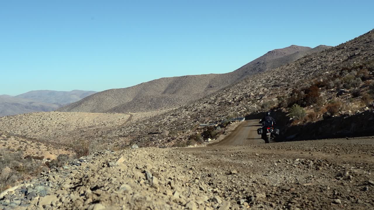 Motociclista solitario si allontana dalla telecamera su una strada sterrata remota, Cile.