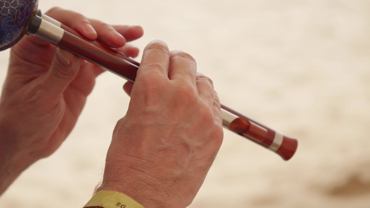 Primer plano de las manos de un músico tocando una flauta de madera al aire libre, mostrando el movimiento de los dedos y la artesanía durante una interpretación de instrumento de viento tradicional.