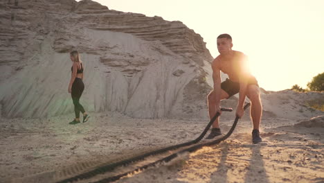 hombre atlético en ejercicio alrededor de las colinas de arena al atardecer golpea la cuerda en el suelo y levantó el polvo.