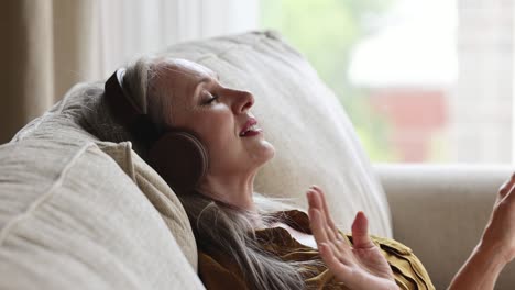 aged female rest on couch in headphones listen to melody