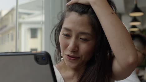 young asian woman having conference call on tablet from coffee shop