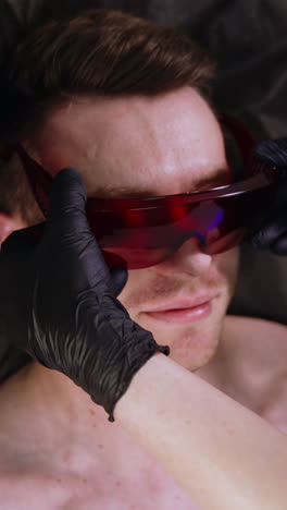 mid-aged caucasian man lies on the bed. specialist in latex gloves puts protective eyeglasses on a male client. vertical video