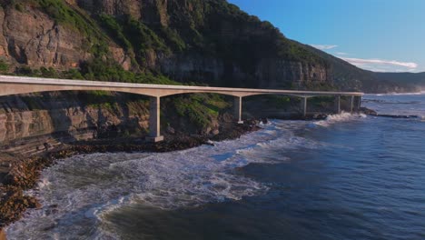 sunrise sea cliff bridge costal drone view iconic famous stanwell park waves ocean crashing south coast nsw australia landscape royal national park wollongong coalcliff iiawarra sydney slow upward jib