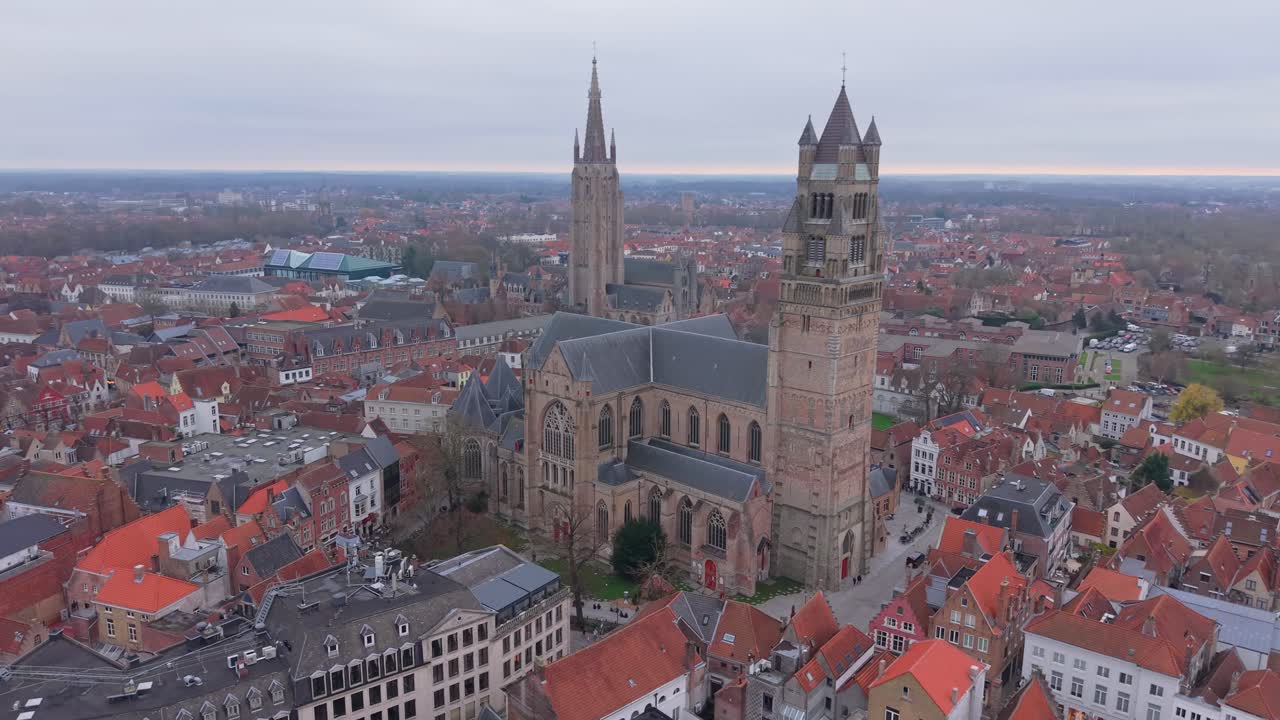 Una ripresa con drone della Chiesa di San Giacomo a Bruges, con i tetti circostanti e la Cattedrale di San Salvatore sullo sfondo, che mostra lo skyline medievale e il carattere storico della città