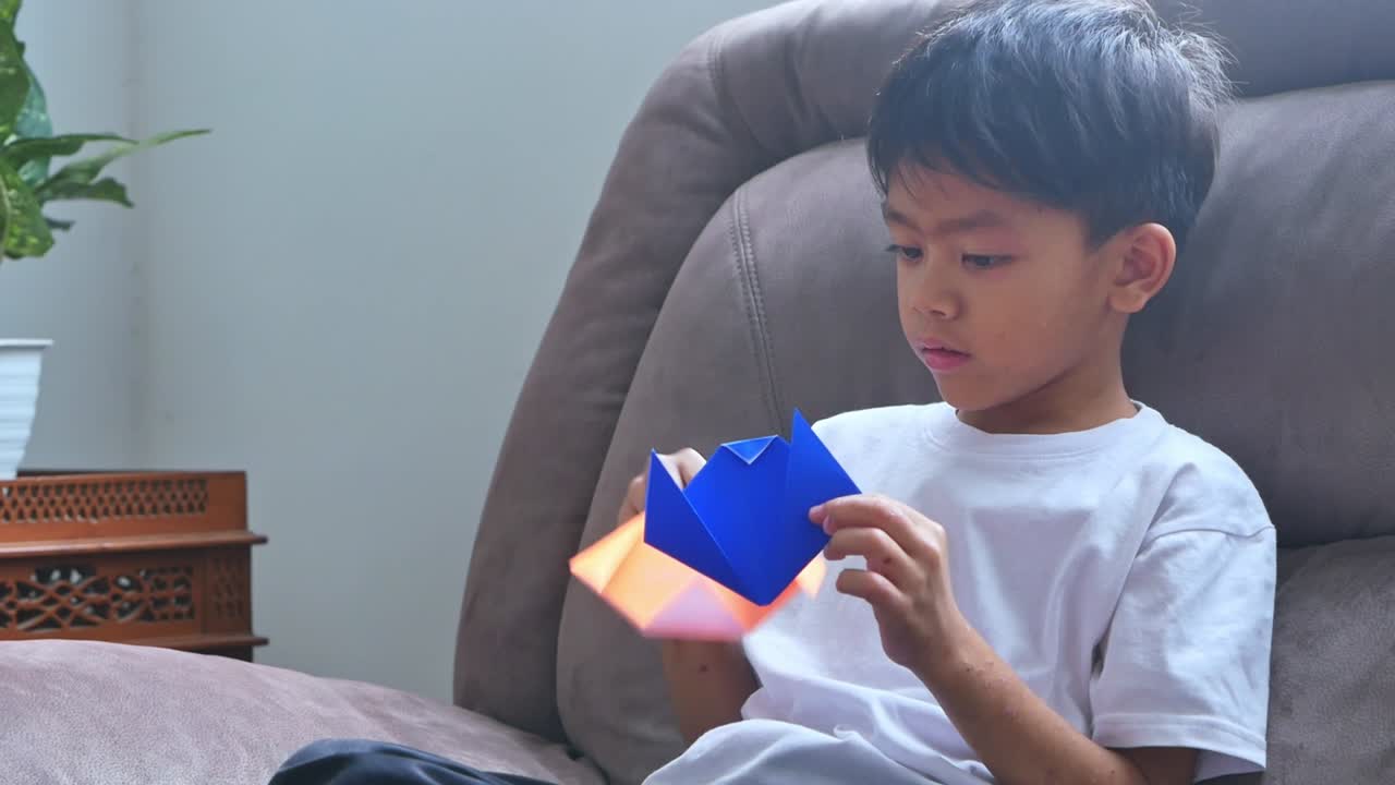 Young boy concentrating intently while playing colorful origami paper on comfortable couch