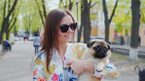 walk with a puppy in the city. young woman with a dog on her hands walking in a city park. steadicam shot