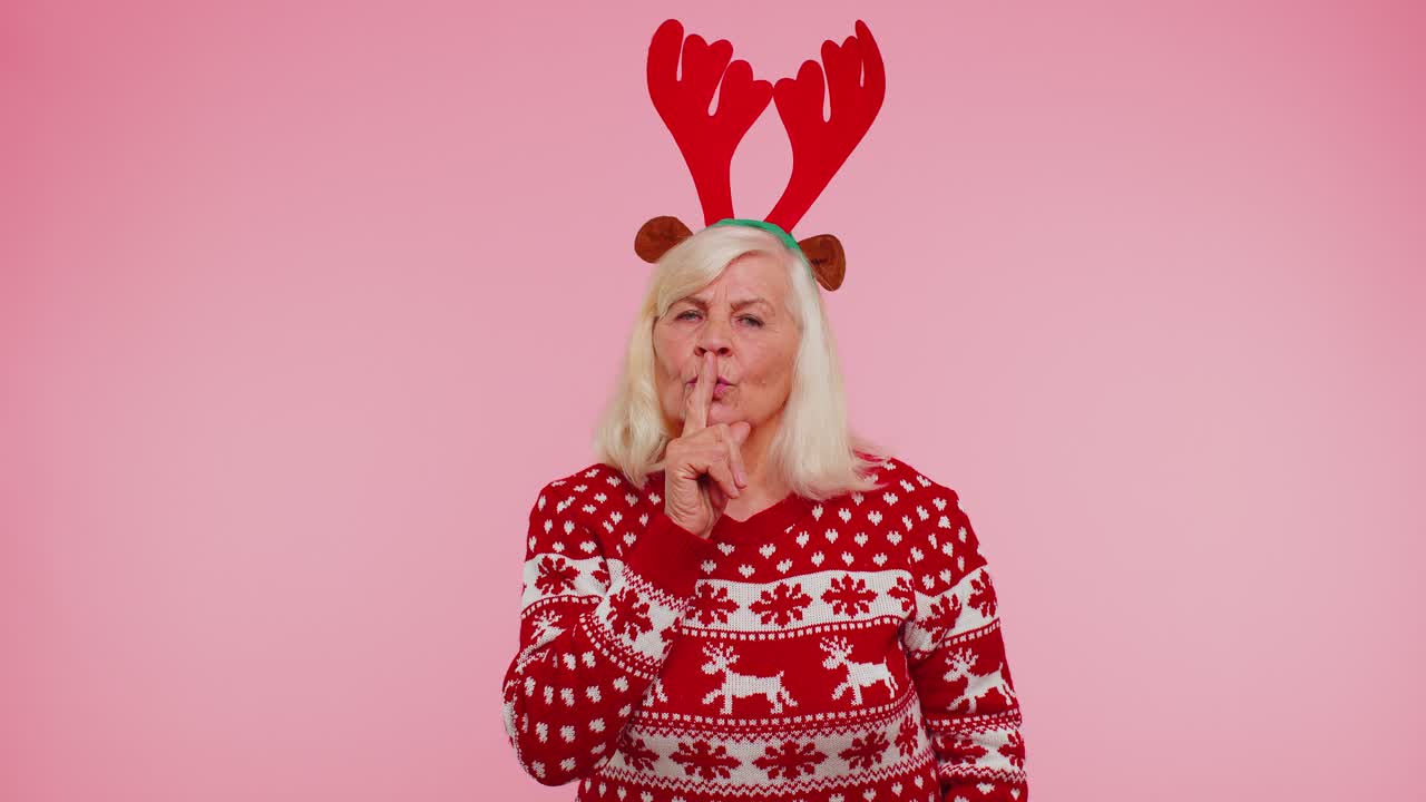 크리스마스 스웨터를 입은 노인이 손가락을 입술에 러 침을 지시하고 신호를 표시합니다.