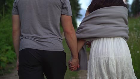 A-couple-holding-hands-and-walking-down-a-path-with-greenery-and-woods-on-Both-sides