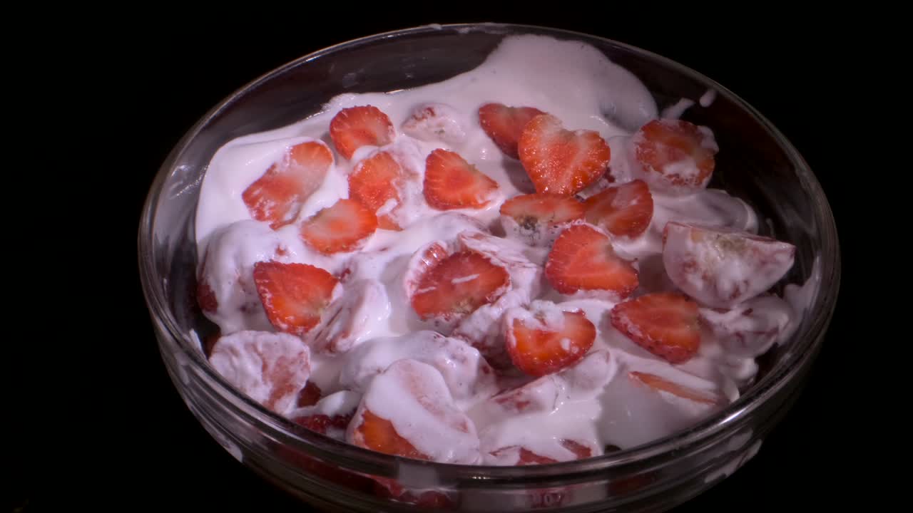 trozos de fresas de jugo cubiertas con una capa de crema en vidrio sobre fondo negro. rotación de la cámara 360 grados, primer plano.