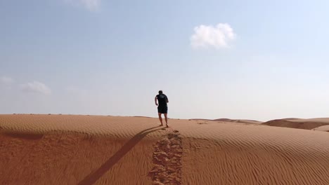 Un-Hombre-Corriendo-Por-Una-Colina-De-Arena-En-El-Desierto,-Cerca-De-Omán