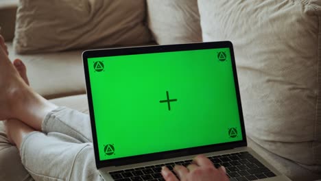 mujer usando una computadora portátil de pantalla verde, tecla de croma, escribiendo y trabajando con el touch pad, acostada en el sofá en casa, cámara zoom