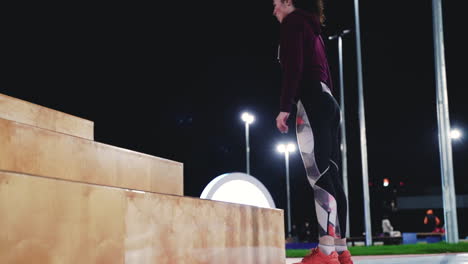 sportive curly girl doing squat jumps on stairs in the park at night