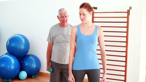 Physiotherapist-showing-elderly-man-how-to-lift-weights